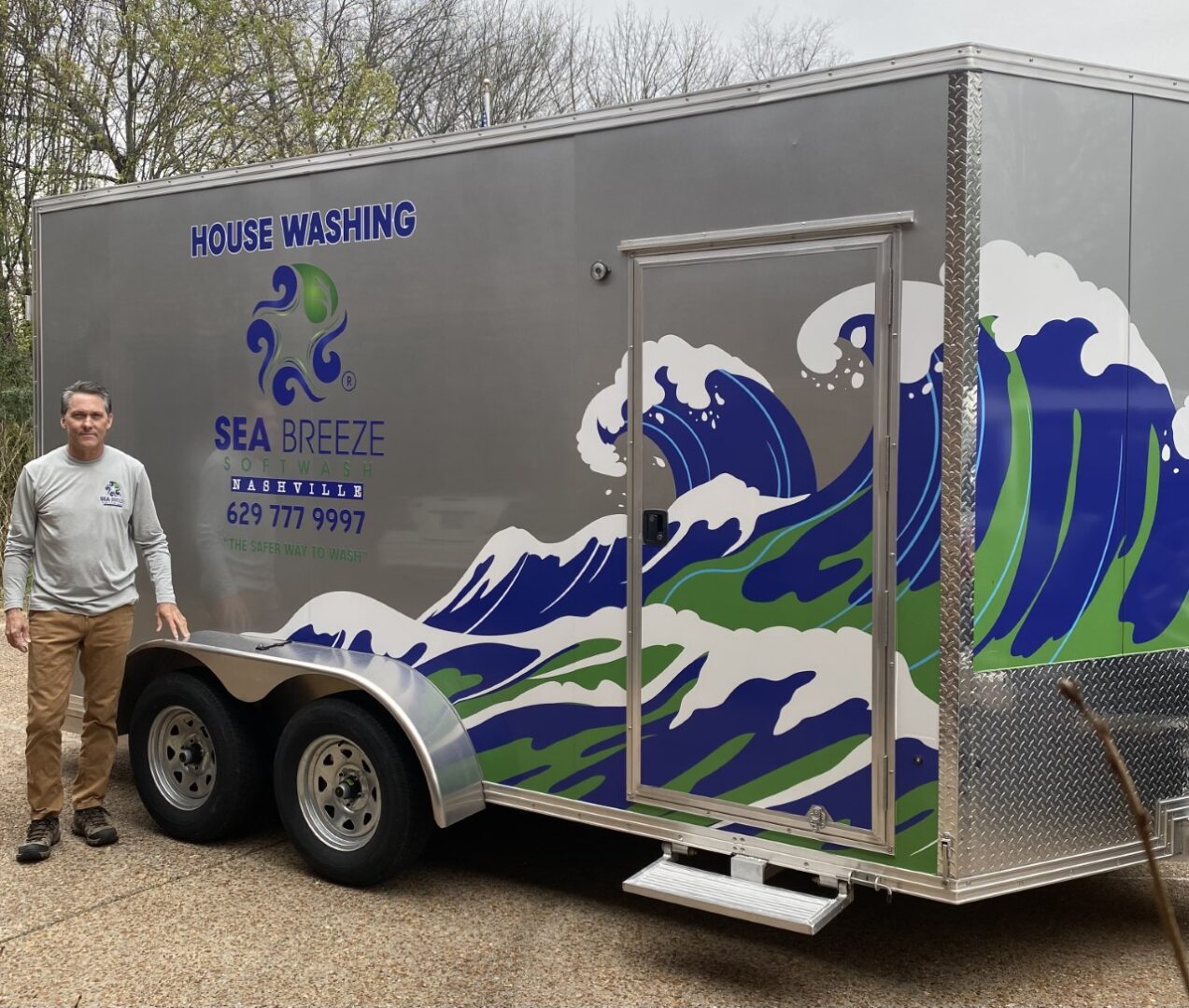 A man standing next to a trailer with waves painted on it.